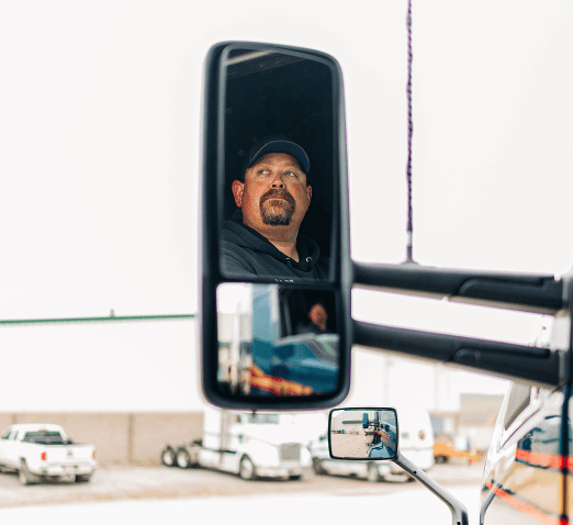 Image of the reflection of a semi driver in the left mirror on a truck.