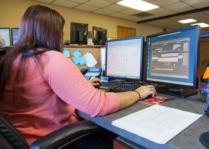 A woman working at a desk with two monitors at Mast Trucking.