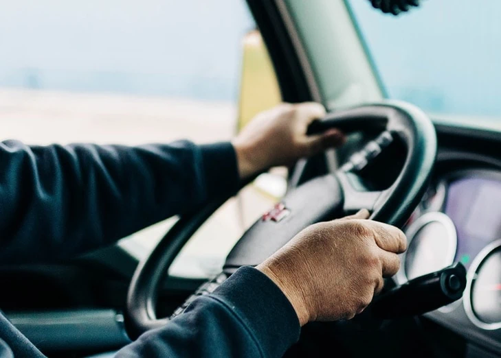 A truck driver operating a truck with his hands on the steering wheel.